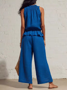 NEWYORKLISTED STYLE COLLECTION: Woman wearing a blue jumpsuit against a white brick wall.
