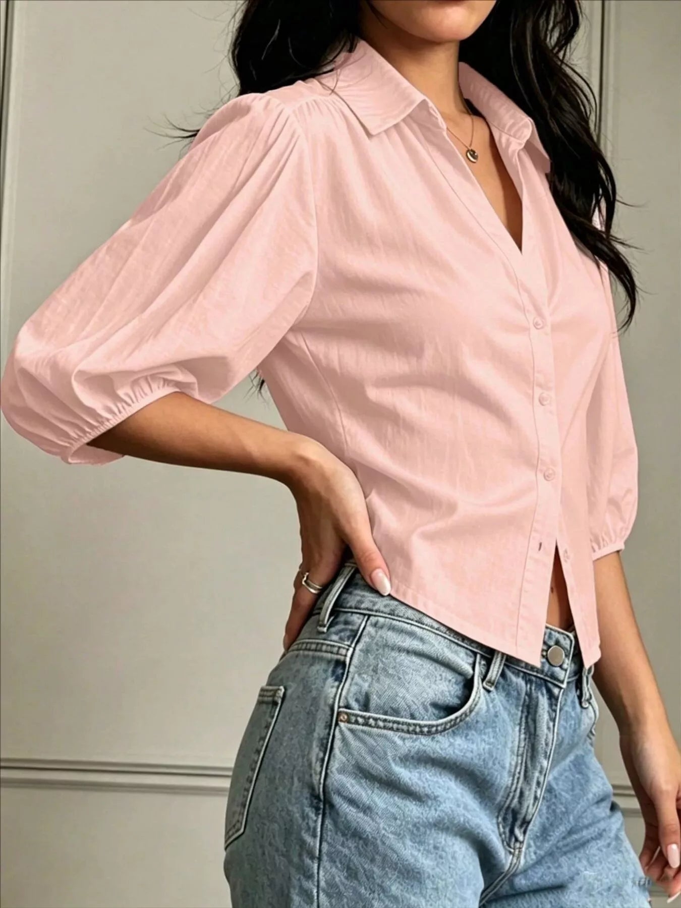 NEWYORKLISTED STYLE COLLECTION: A woman wearing a light pink button-up blouse with voluminous elbow-length puff sleeves and light-wash blue jeans, shown from the neck down against an indoor wall background.