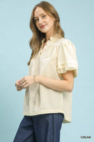 NEWYORKLISTED Style Collection: Woman wearing a cream blouse with ruffled sleeves against a light blue background